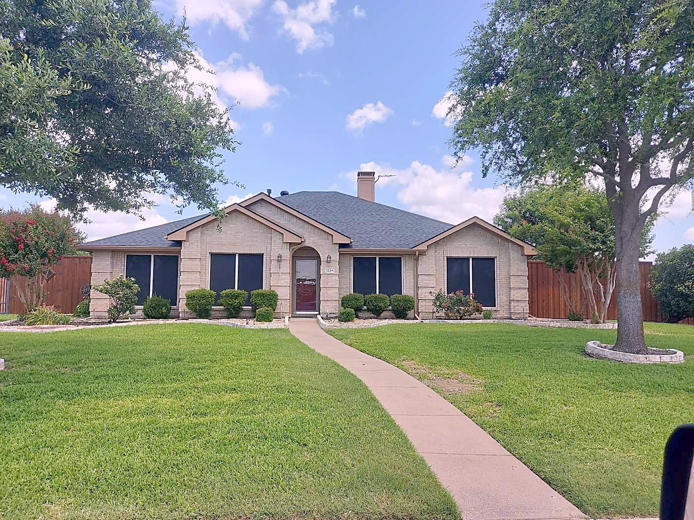 Front of a single-story brick home with a gray shingle roof and a long front walk