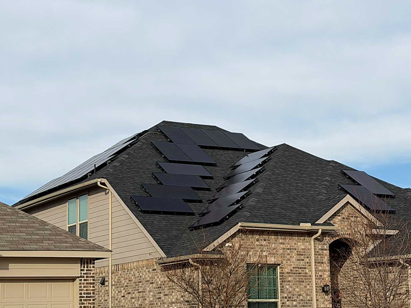 Solar panels set back on a dark shingle roof over a brick and siding home