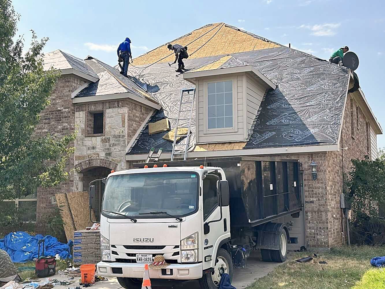 A crew tearing off an old roof with a dump truck parked in the driveway