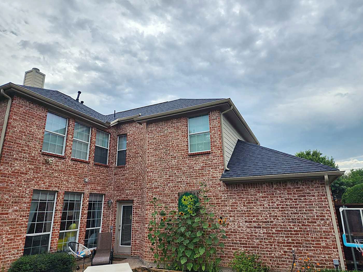The back of a two-story red brick home with a new shingle roof